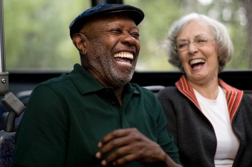 An-elderly-mixed-race-couple-sitting-on-a-bus-together-laughing